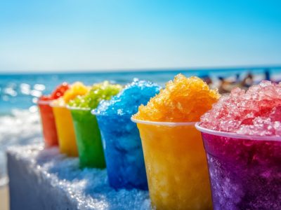 Colorful cups of shaved ice lined up on a table next to the beach with a clear ocean view in the background Colorful cups of shaved ice lined up on a table next to the beach with a clear ocean view in the background